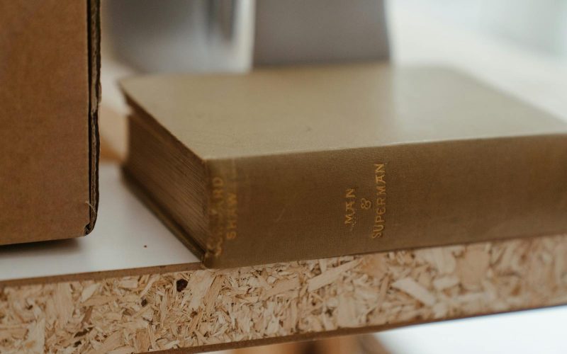 Close-up of a vintage book titled 'Man & Superman' placed on a wooden shelf indoors.